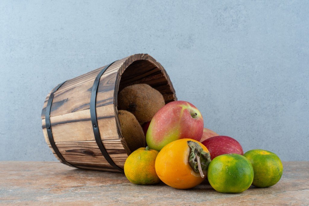 A wooden basket with fresh sweet fruits on gray background